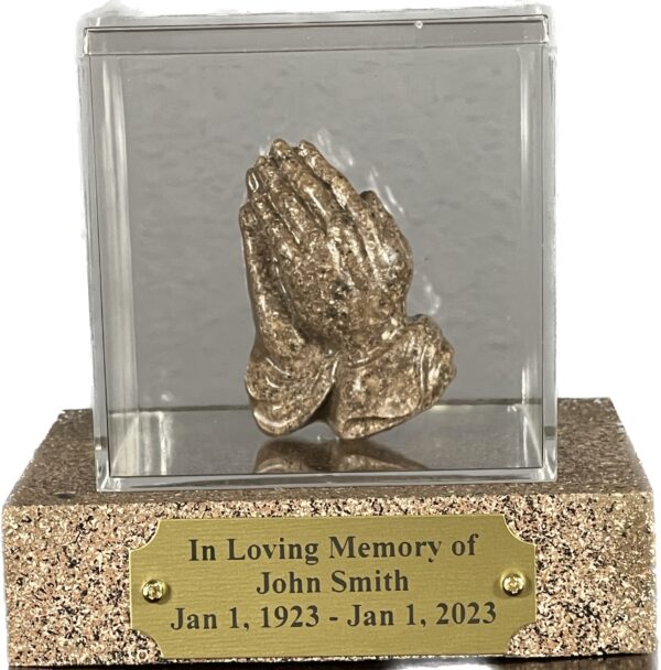 Prayer Hands made from cremation ashes enclosed in an acrylic glass container. They sit on top a wooden base with the names engraved in a bronze plaque.